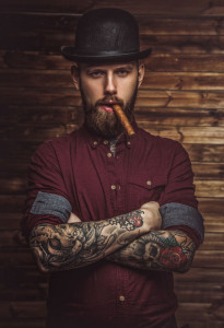 58123976 - bearded man with tattooes on arms smoking cigar.